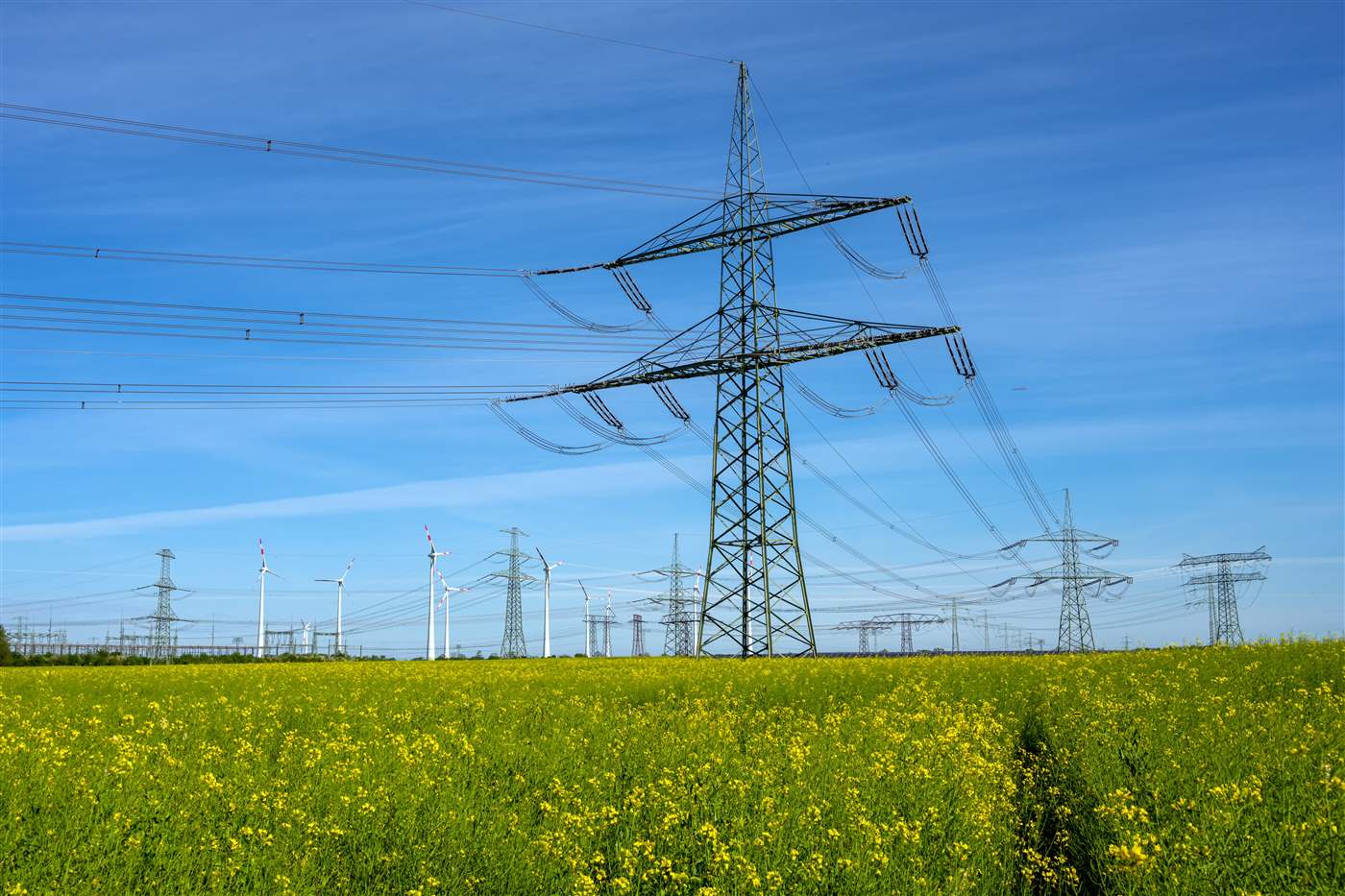 Linie i słupy wysokiego napięcia obok turbin wiatrowych - przyłączenie projektu OZE do sieci